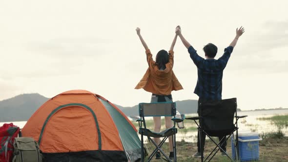 Young Asian couple cheering and celebrating successful climb on setting camping.