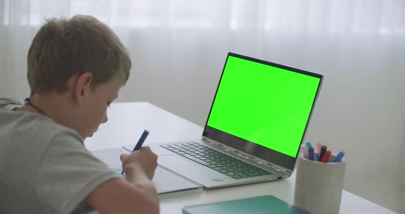 Little Boy Is Learning Remotely, Viewing Video on Laptop and Drawing on Paper By Pencil, Chroma Key