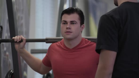 Tight shot of a man doing squat lifts while friend watches.