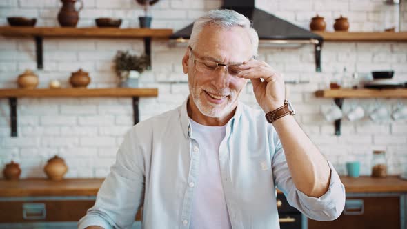 Grayhaired Businessman is Taking Off Glasses and Smiling Having Rest Sitting at Table of Modern