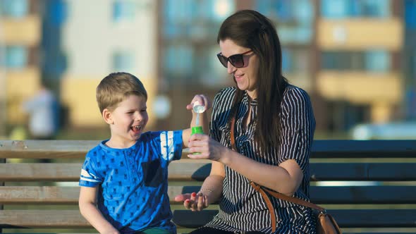 Happy Child and Woman Playing with Soap Bubbles in Park