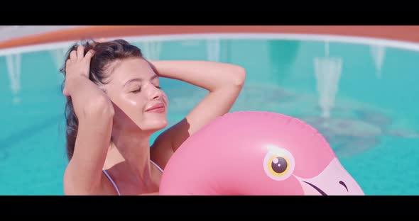 Positive Woman Swimming on Inflatable Flamingo in Pool