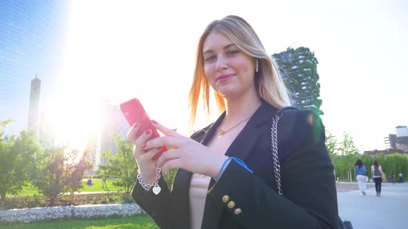 Attractive businesswoman using red smartphone for video call in park