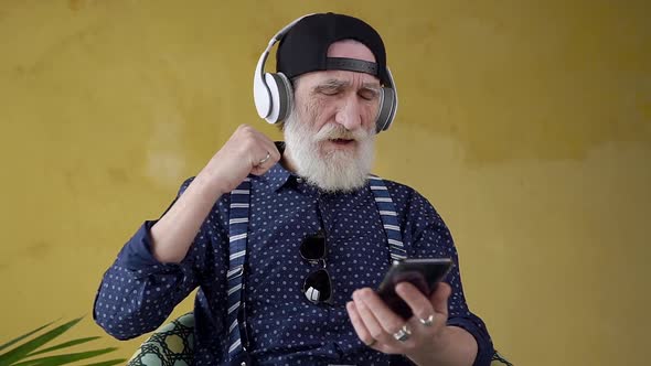 Bearded 70-aged Man Listening Modern Music in Headphones