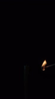 A candle is lit with a match on a black background. Vertical video.