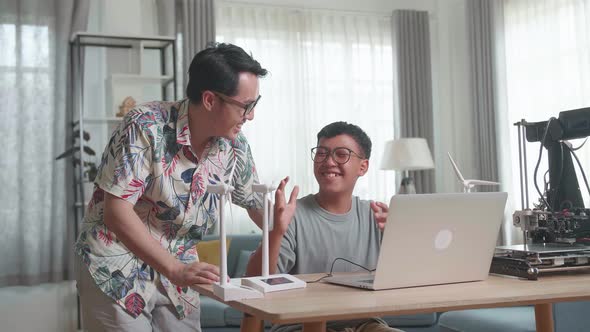 Cheerful Father And His Son Using Laptop Computer Programming Electric Wind Turbine Model