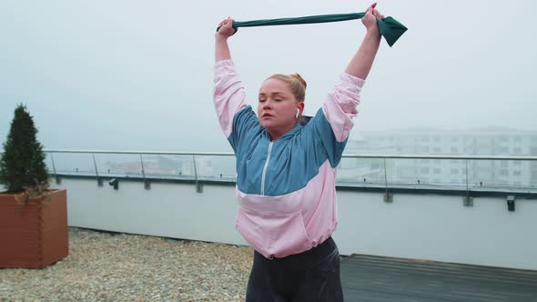 Sporty Girl in Sportswear Does Yoga Stretching Exercising Using Rubber Band on Roof of House Outdoor