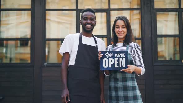 Slow Motion Portrait of Man and Woman Business Partners Holding Cafe Open Sign and Smiling Looking