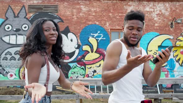 Black Guy And Girl Dancing On The Street. They Are On Graffiti Wall Background.