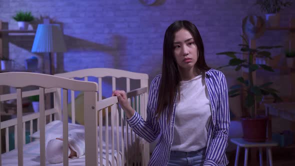 Tired Sad Young Asian Mom Rocks a Baby Cot