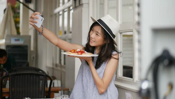 A young Asian girl takes a photo with pancake at a cafe shop.
