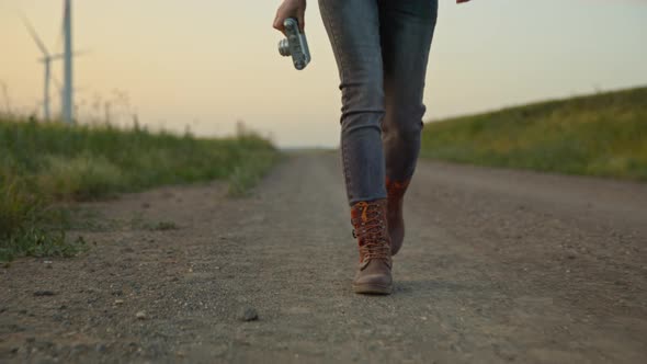 Young photographer in boots near the road with a farm with alternative energy windmills