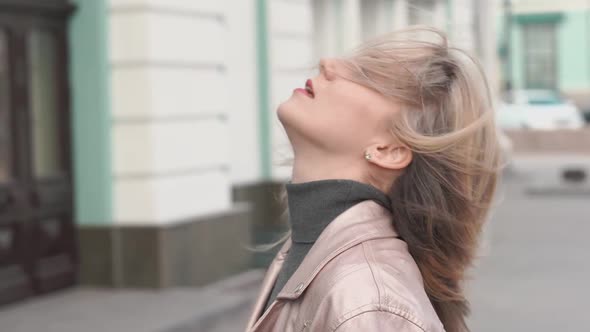 Young Beautiful Blonde Woman in Pink Jacket Spinning in the Center of a City