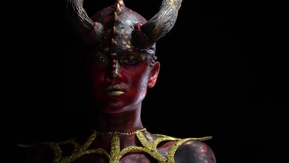 Close up of a demon with red and black skin with scales and long horns