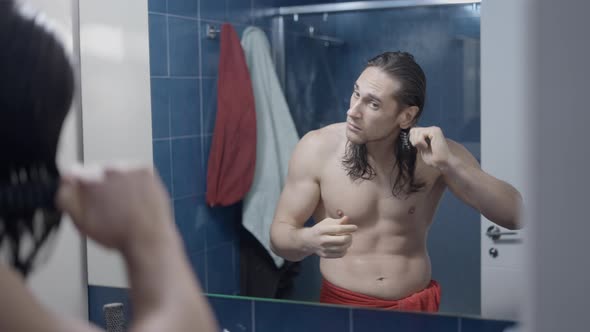 Young Caucasian Pretty Man Brushing His Hair After a Shower in Front of a Mirror  Middle Shot