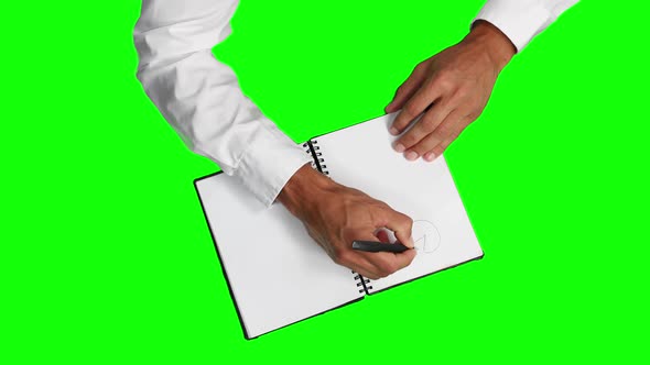 Overhead view of a caucasian man drawing graphs in a notebook with green screen