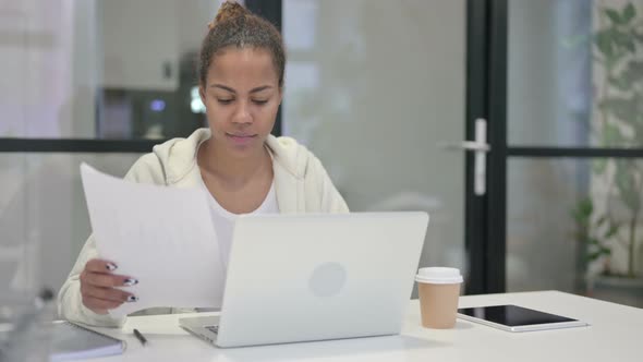 African Woman with Laptop Having Loss While Reading Documents