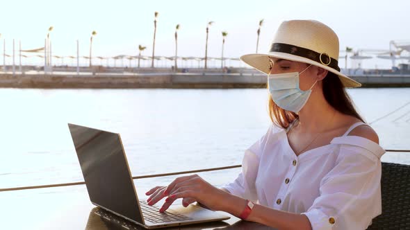 Young Woman in Protective Mask, Sun Hat and Summer Clothes, Working on Laptop, Sitting on an Empty