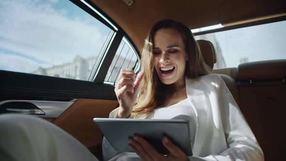 Surprised Business Woman Reading Good News on Tablet Computer in Luxury Car