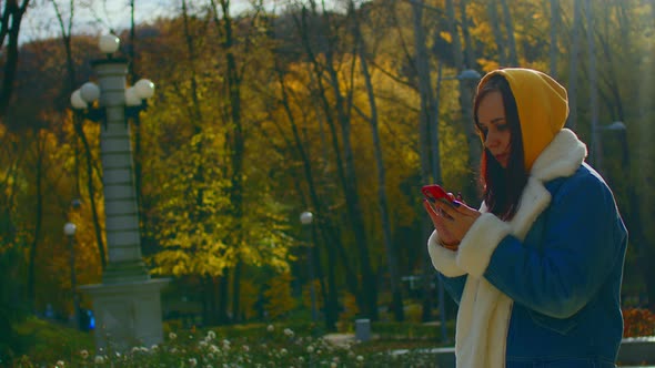 Young Woman Standing with Mobile Phone in City Park