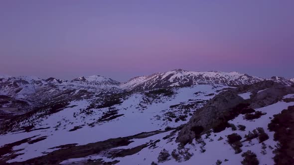 Flying over tops of snow-covered mountains in winter at dusk. Aerial