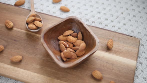 Top View Of Almonds On Wooden Board Falling In Wooden Bowl. Slow Motion.
