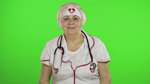 Elderly Caucasian Female Doctor in Protective Mask. Waving Her Hands alt