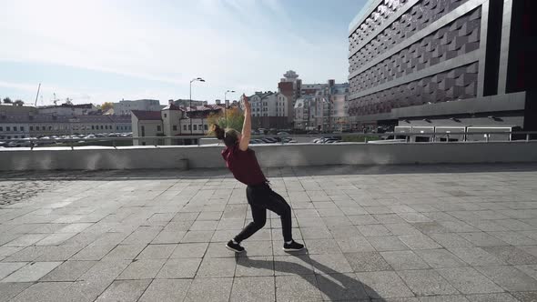 Young Female Gymnast Doing a Series of Flips and Runs on Training Area Near Modern Buildings