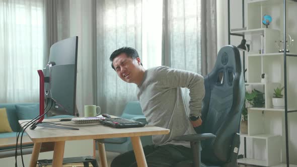 Asian Man Having Backache While Using Desktop Computer For Working At Home