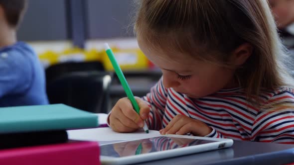 Cute schoolgirl drawing pictures in classroom