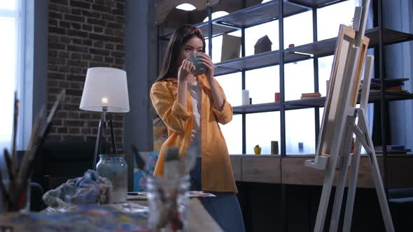 Happy Female Painter Admiring Artwork in Workshop