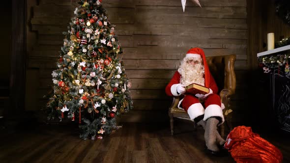 Santa Claus Pulling Out Reading Book Near Christmas Tree at Home
