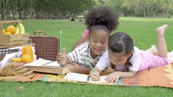 Two little girl writing and doing homework on notebook together while sitting and lying on mat 