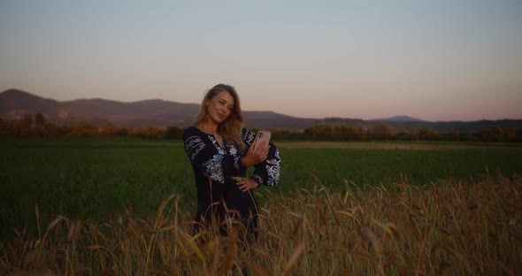 Young woman in national Ukrainian clothes standing on a wheat field  at sunset or sunrise