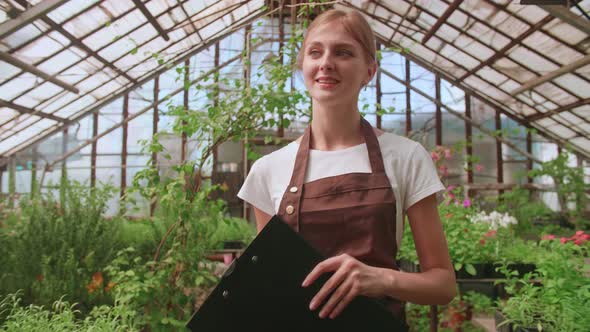 Female Gardener Checks Quality of Plants Takes Notes on Digital Tablet Walking Along Garden Center