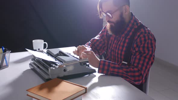 Writer's Day Concept. Young Male Writer in a Dark Room Typing on a Typewriter