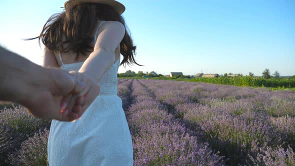 Smiling Woman in Hat Holding Male Hand and Jogging Through Lavender Field