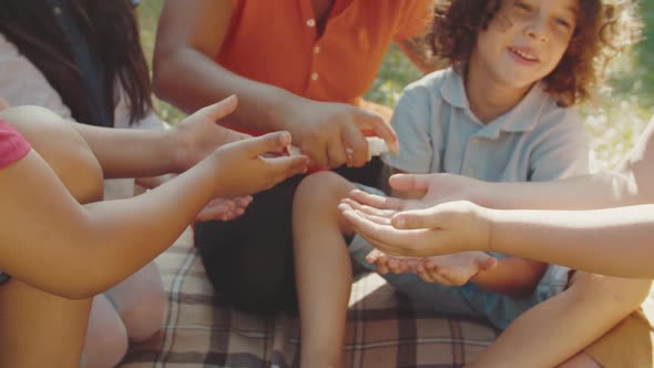 Charming Teacher Applying Hand Sanitizer to School Children Outdoors