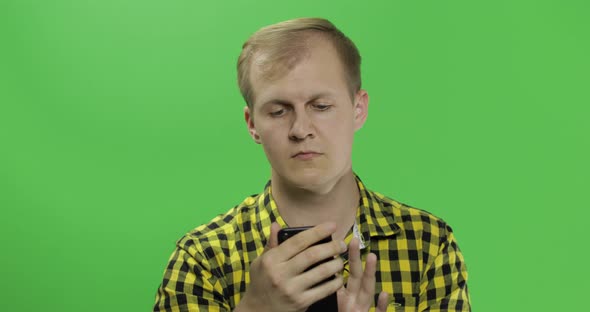 Caucasian Man in Yellow Shirt Scrolling Texting on the Smartphone in His Hands