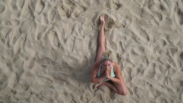 Overhead shot of a young attractive woman doing yoga on the beach