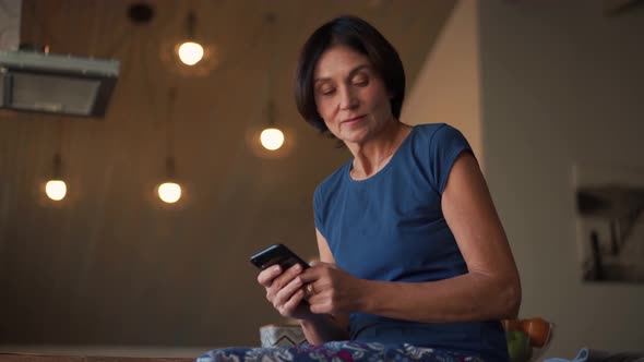 Positive mature woman looking at phone and to side