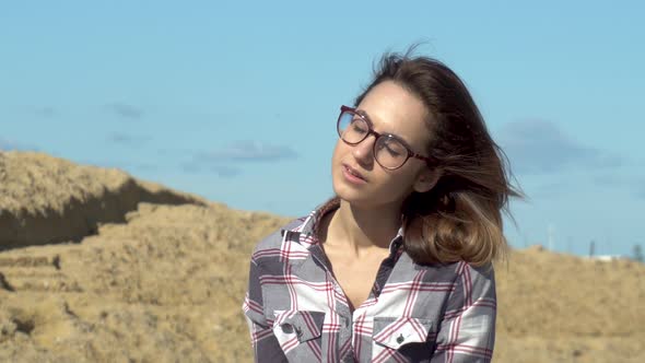 A Young Woman Sits on Stones on a Background of the Sea. The Wind Blows on the Girl Hair