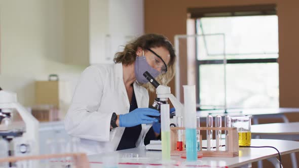 Female teacher wearing face mask using microscope at laboratory at school