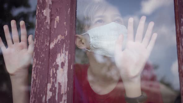 Boy in Mask Inside Looks at the Window and Takes Off the Mask