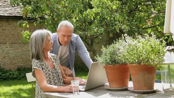 WS, Senior couple at table in garden looking at laptop computer