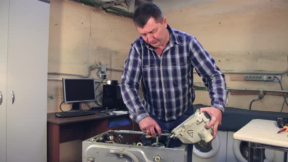 A Male Specialist Disconnects a Part of a Washing Machine