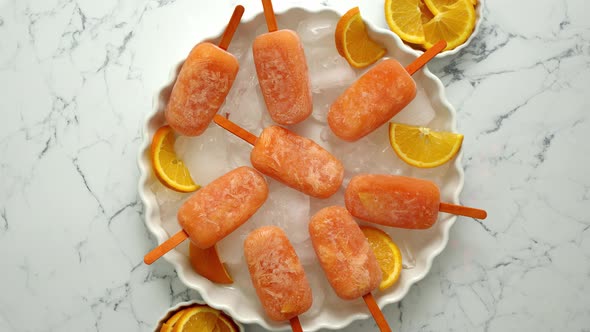 Homemade, Juicy, Orange Popsicles. Placed on a White Plate with Ice Cubes