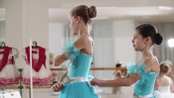 Little Girl Ballerina Fixing Her Hair and Her Friend Helps Her with Her Costume