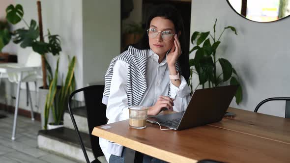 Happy young brunette woman in eyeglasses working on laptop