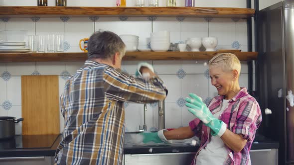 Portrait of Joyful Elderly Couple Washing Dishes and Playing with Foam Having Fun